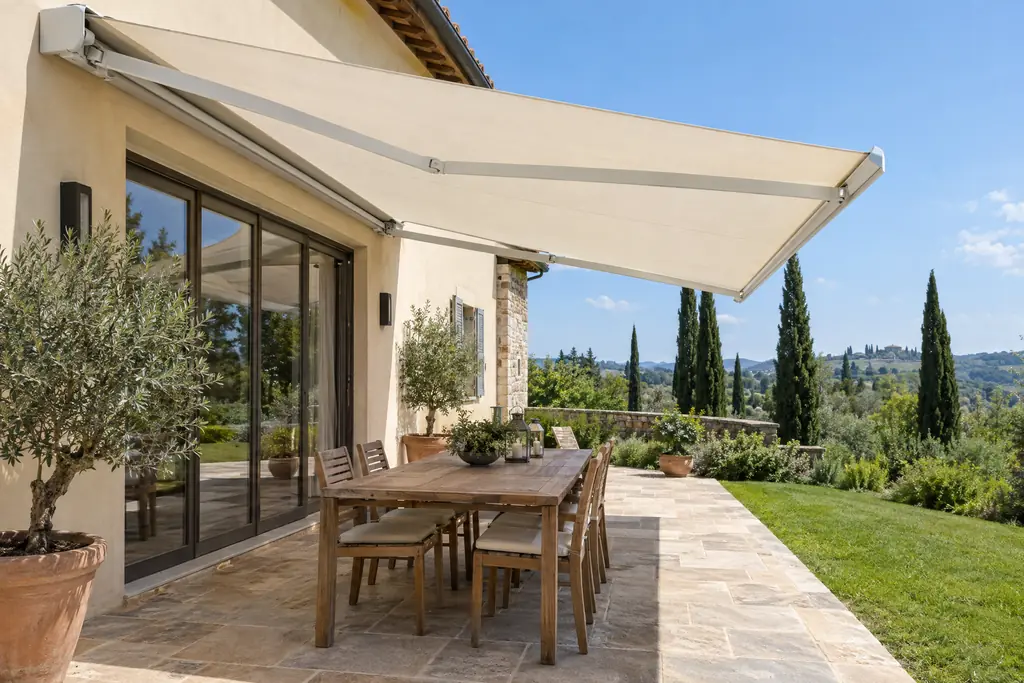 Terrazza di una villa italiana con una tenda da sole a bracci aperta sopra un tavolo apparecchiato